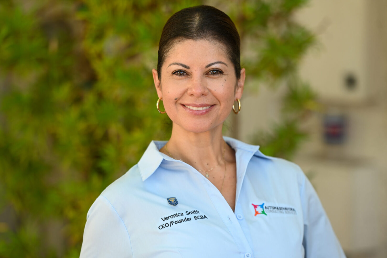 Woman in a light blue shirt smiling against a green background.